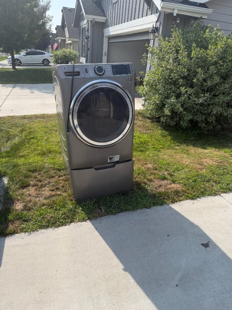 GE front-load dryer on a pedestal sitting on the front lawn awaiting appliance removal in Meridian, Idaho