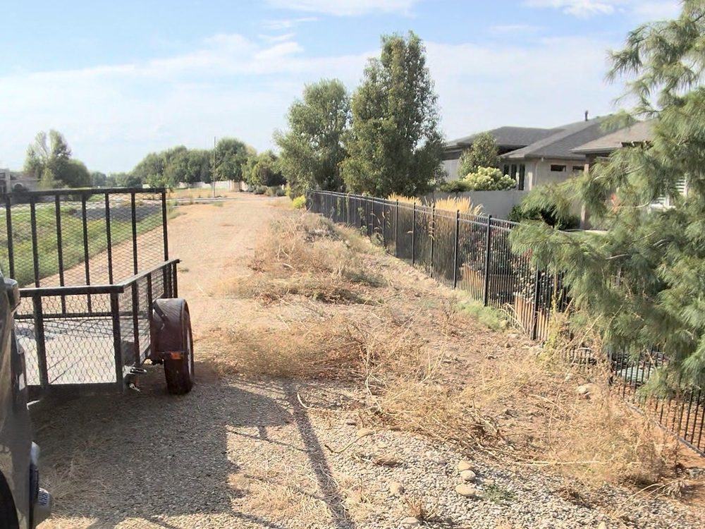 Overgrown weeds, dead brush and tumbleweeds choking a gravel strip along a fence line in Meridian, Idaho before HaulWorks cleared it
